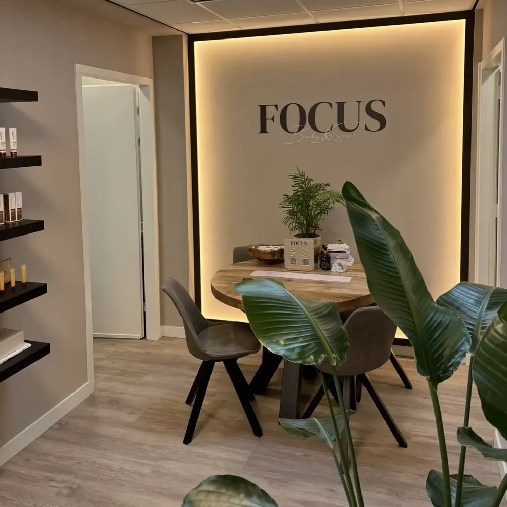 Het warme, rustgevende interieur van de salon FOCUS Body & Soul met tafel, stoelen, een plant en zacht licht.